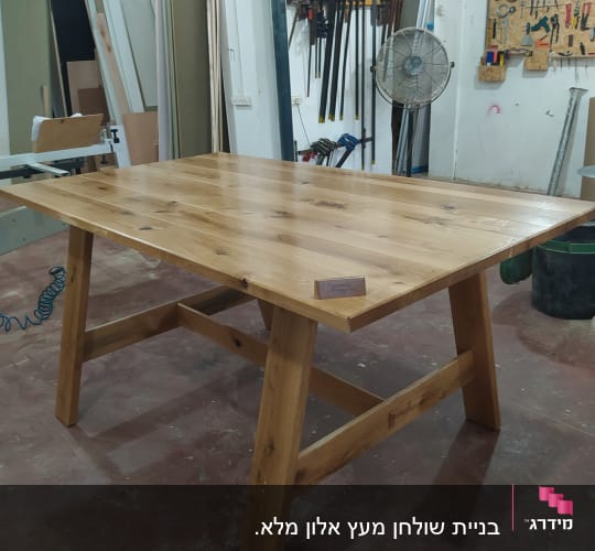 שולחן עץ גמור בסדנת נגרות עם כלים על הקיר